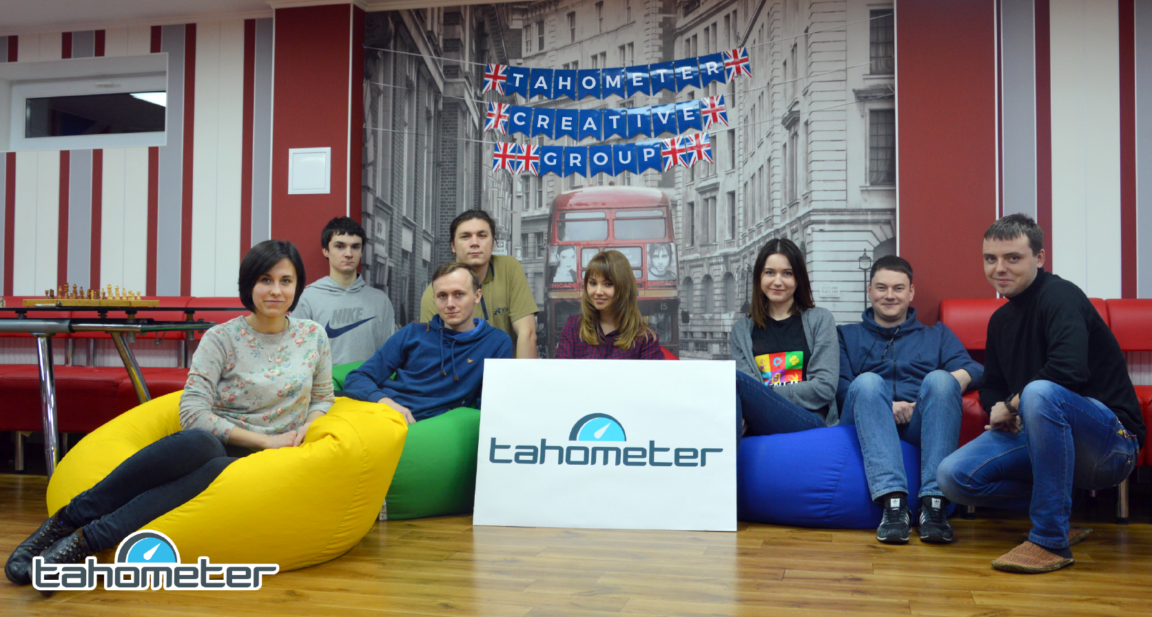 Tahometer Creative Group team posing with logo sign and colorful bean bags in modern office space.